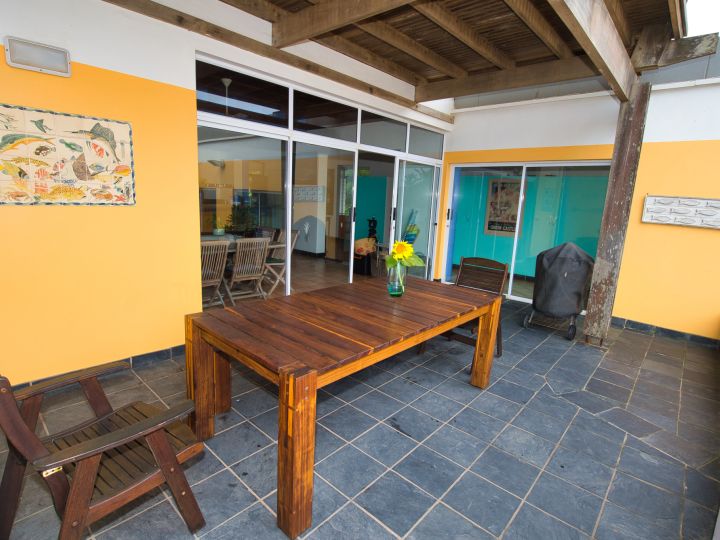 Outside deck area. Open roof, yellow walls, wooden furniture, dark grey tiling.