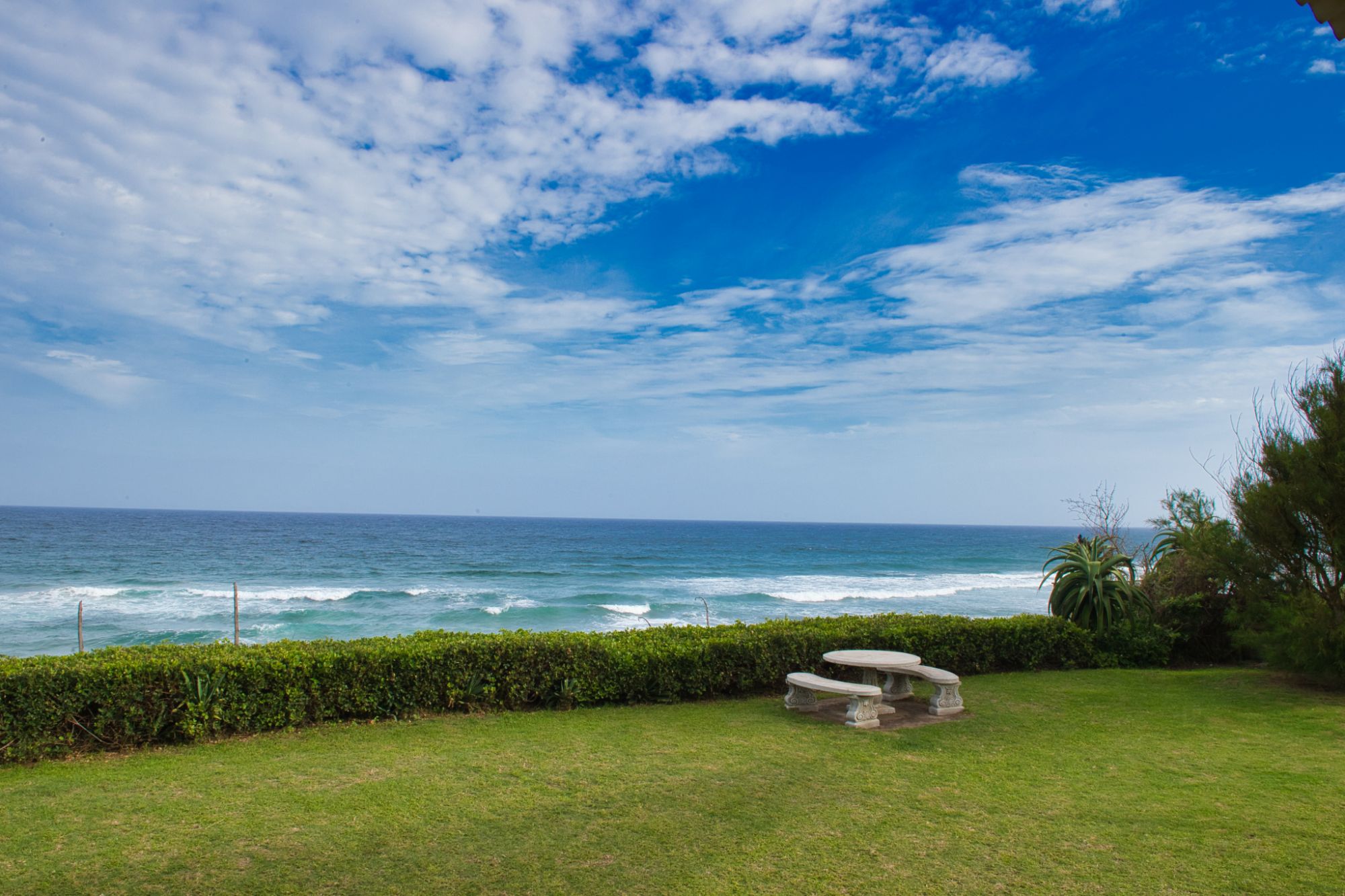View from holiday home, left side. The front yard is displayed, with cemented garden furniture and the ocean just beyond that.